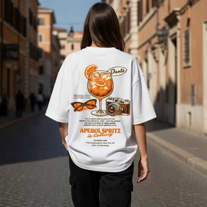 Person wearing a white t-shirt with Aperol Spritz graphic on a street.
