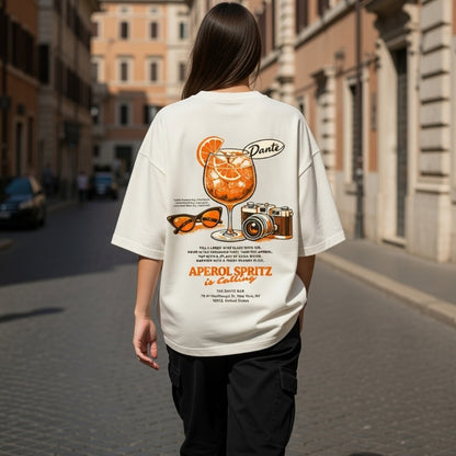 Person wearing a white t-shirt with a drink graphic and text on a city street.