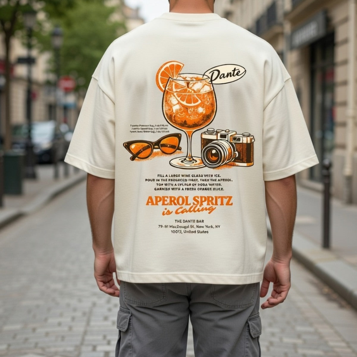 Person wearing a t-shirt with a graphic of an Aperol Spritz cocktail and text on a city street.