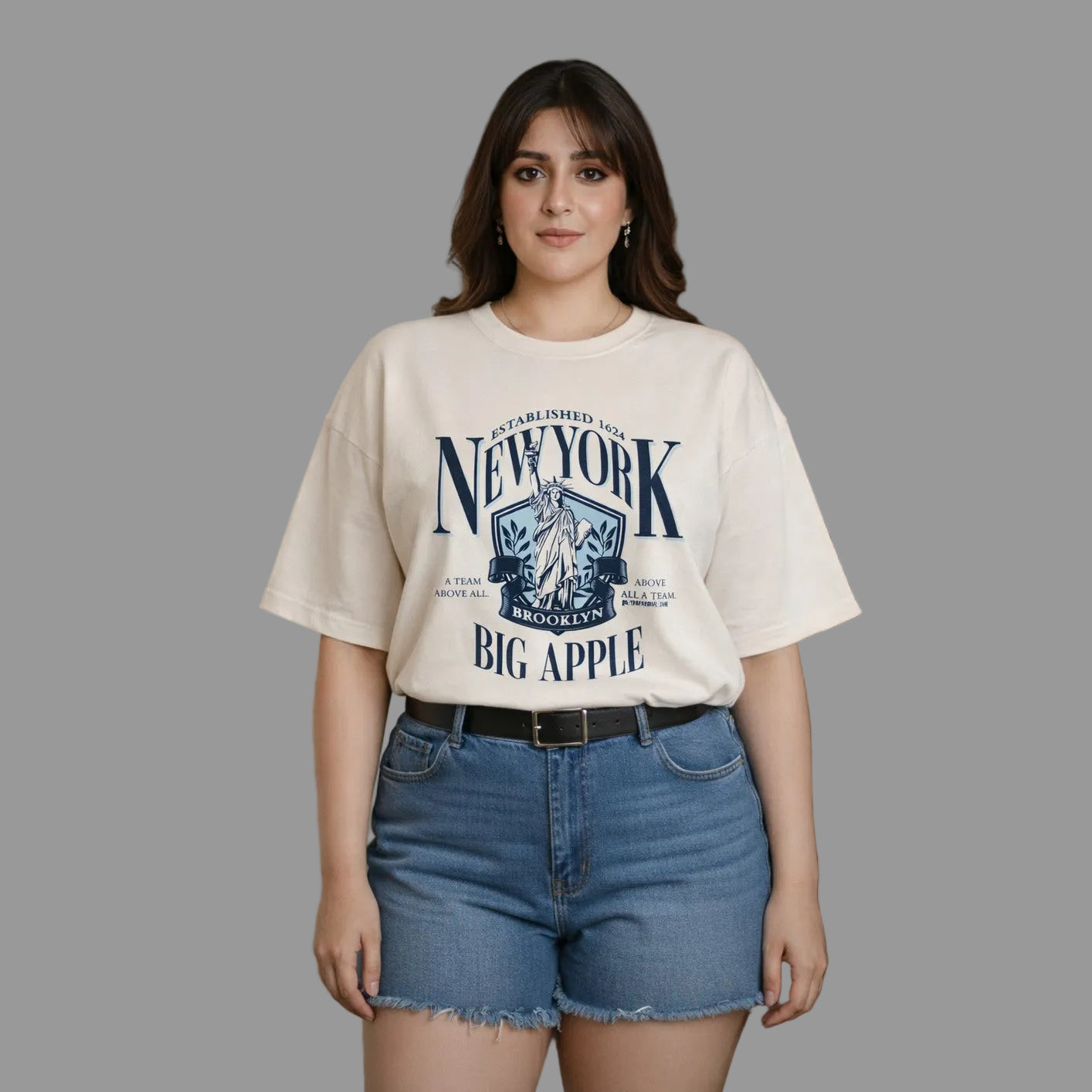 Woman wearing a 'New York Big Apple' t-shirt and blue shorts against a neutral background