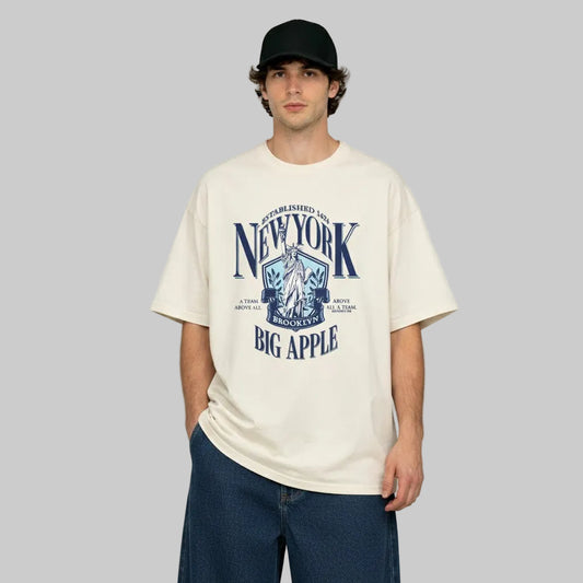 Person wearing a cream t-shirt with 'New York Big Apple' graphic design on a plain background