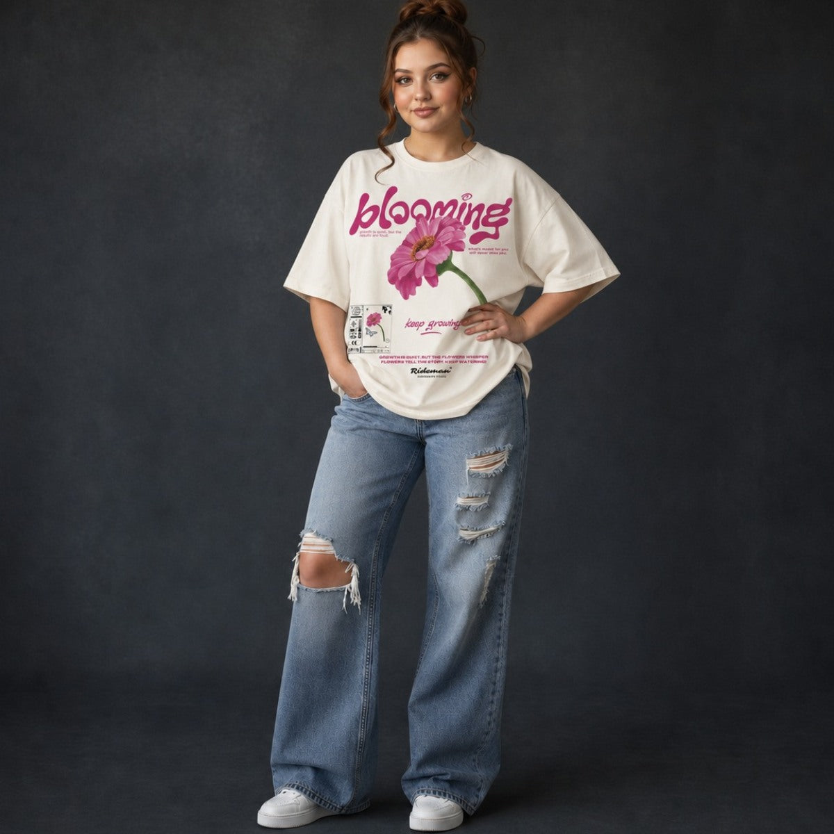 Person wearing a white oversized t-shirt with floral design and text, paired with ripped jeans on a dark background