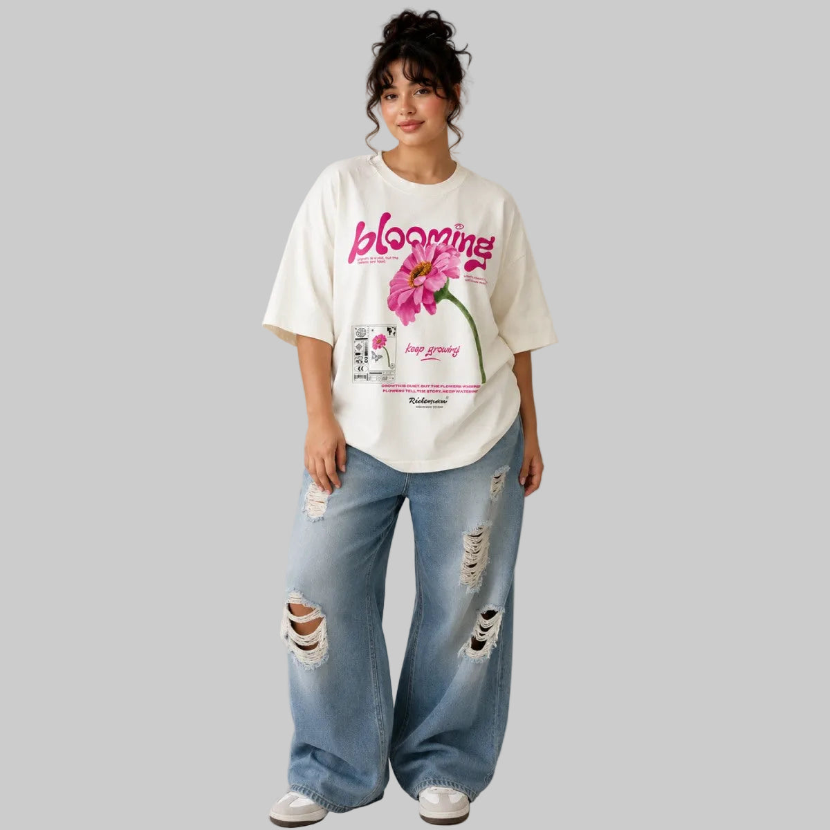 Person wearing a white t-shirt with a floral design and text, paired with ripped jeans on a plain background