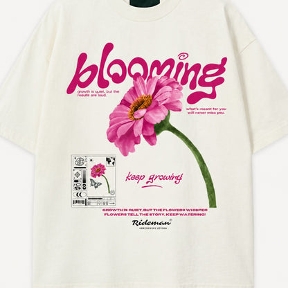 White t-shirt with pink flower graphic and 'blooming' text on a white background