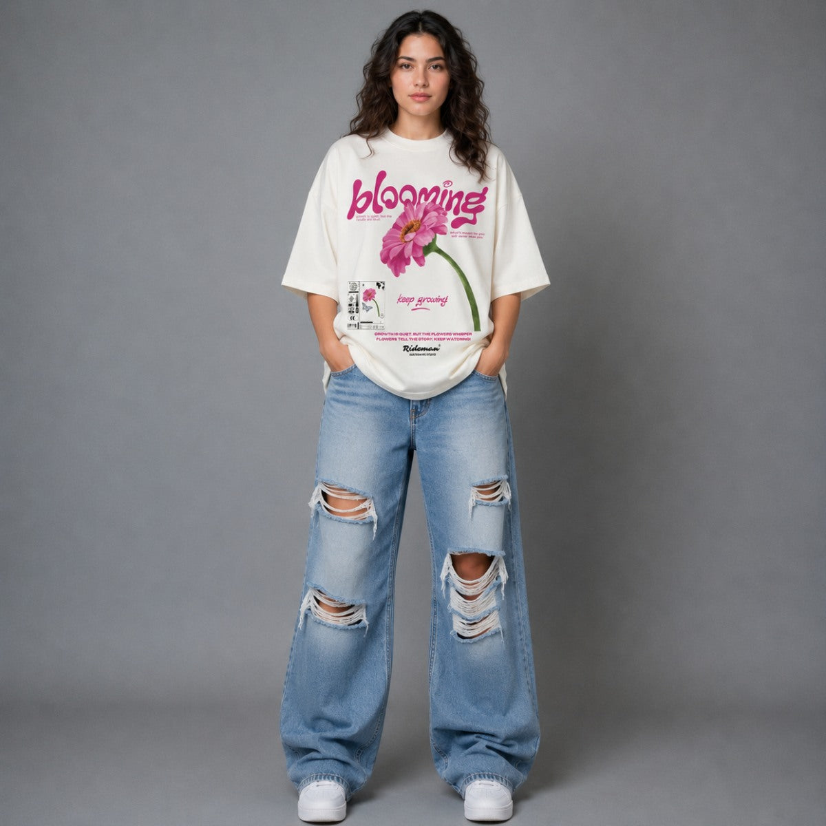 Person wearing a white t-shirt with a graphic design and ripped blue jeans on a gray background
