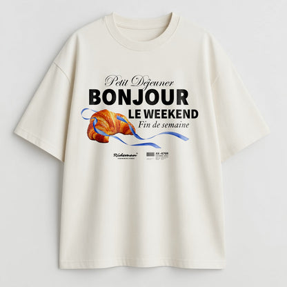 White t-shirt with a graphic design featuring text and a croissant on a light gray background