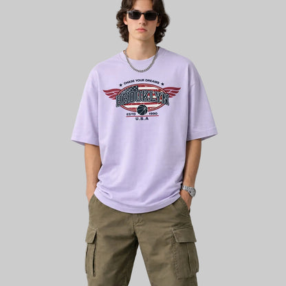Person wearing a light purple t-shirt with a graphic design and green cargo pants on a plain background