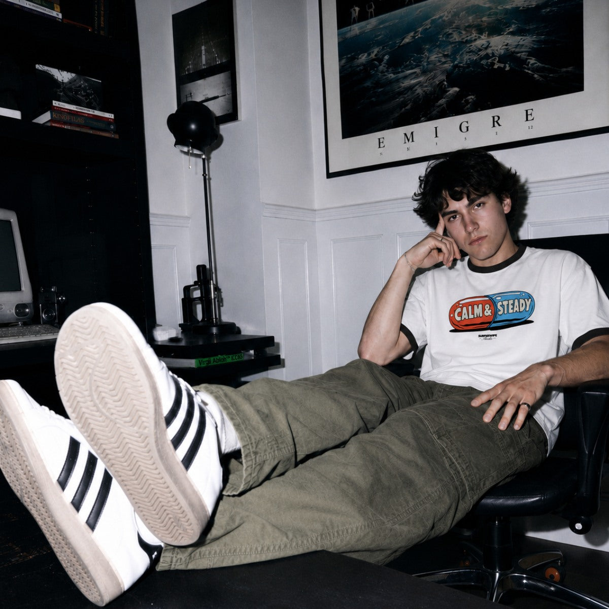 Person sitting in a chair with feet up, wearing a 'Calm & Steady' t-shirt, in a room with decor elements.