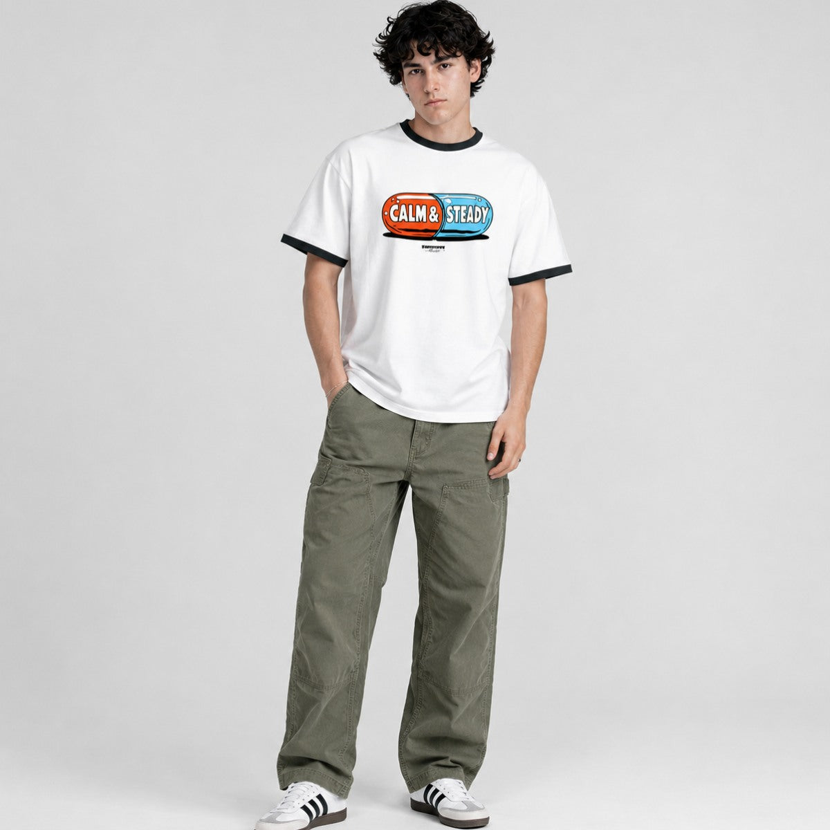 Person wearing a white t-shirt with a colorful graphic and text, paired with green pants on a light gray background.