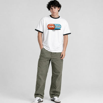 Person wearing a white t-shirt with a colorful graphic and text, paired with green pants on a light gray background.