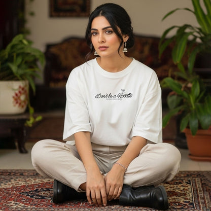 Woman sitting cross-legged on a rug wearing a white t-shirt with text, surrounded by plants.