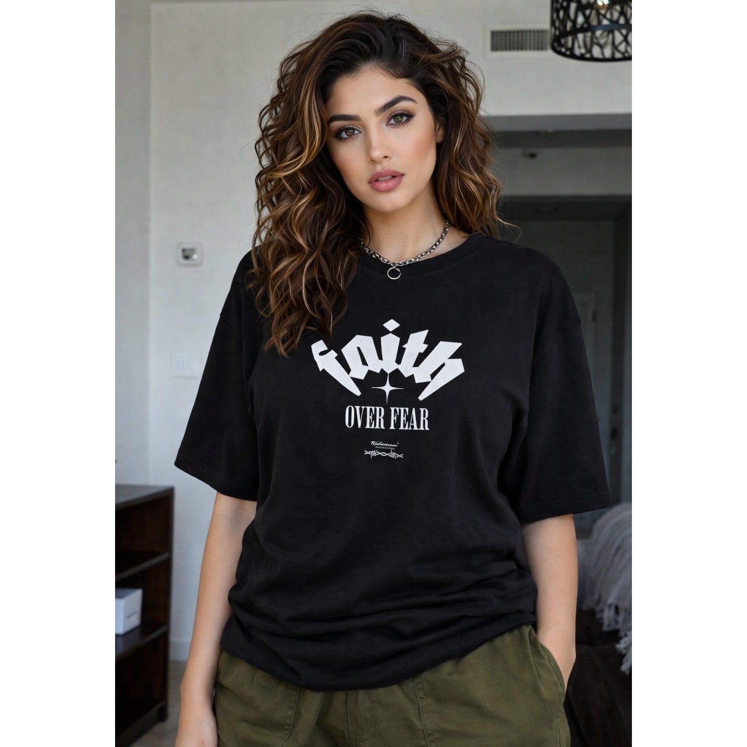 Woman wearing a black t-shirt with 'Faith Over Fear' text in a casual setting.