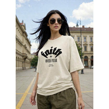 Woman wearing a beige t-shirt with 'Faith Over Fear' text in an urban setting