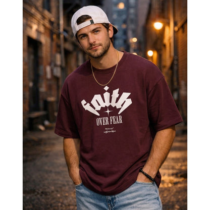 Man wearing a maroon t-shirt with 'Faith Over Fear' text in an urban alleyway.