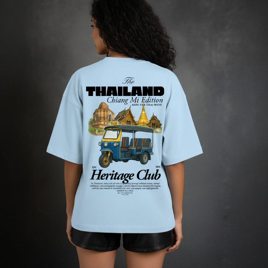 Person wearing a light blue t-shirt with a graphic design on the back, featuring text and images of a tuk-tuk and temples.