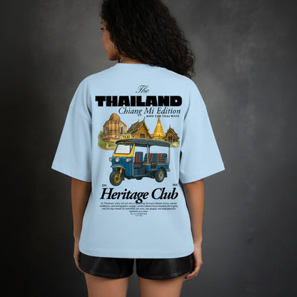 Person wearing a light blue t-shirt with a graphic design on the back, featuring text and images of a tuk-tuk and temples.