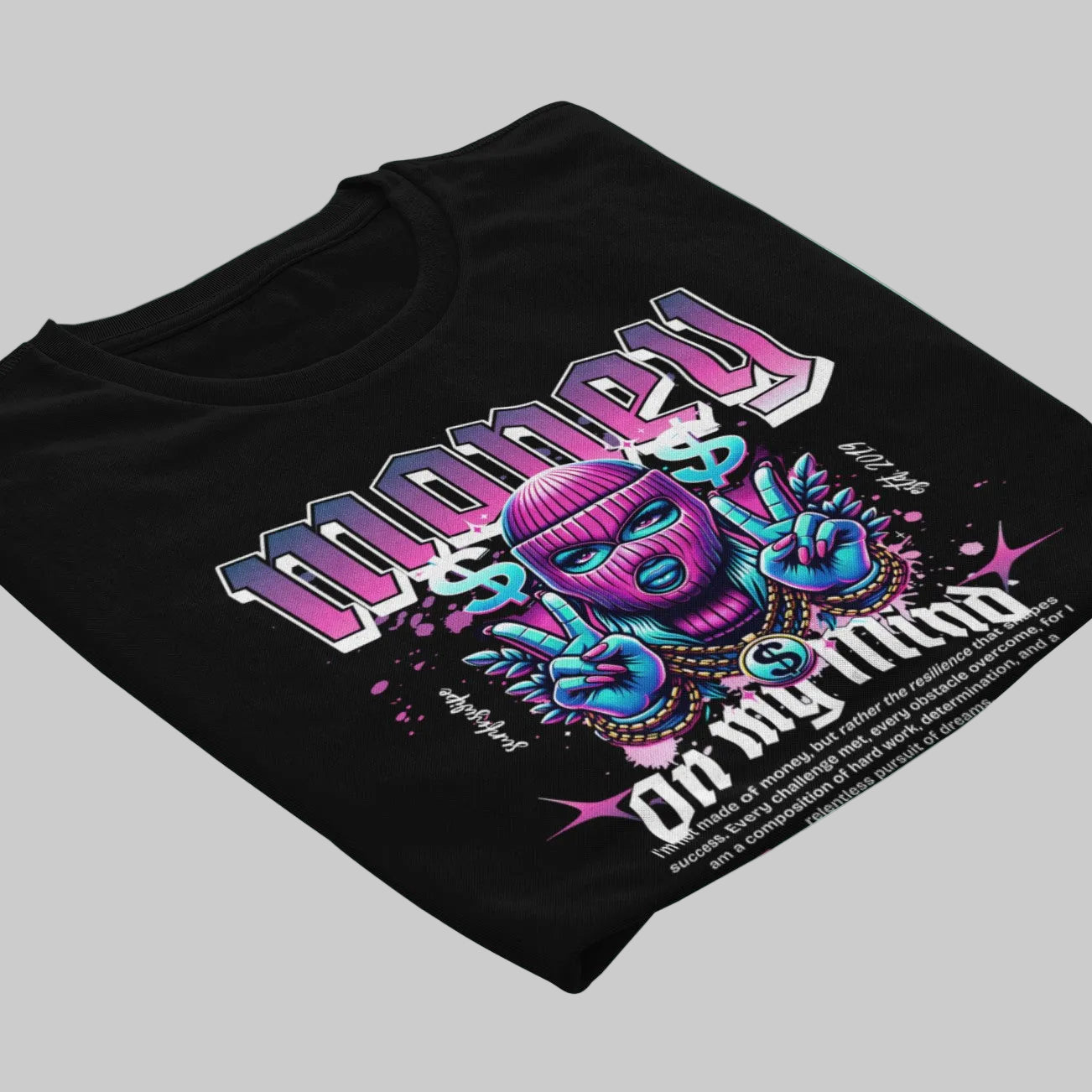 A black short-sleeve t-shirt laid flat on a light gray background, featuring a colorful graphic print with the text 'Money $ My Mind' and a stylized purple and blue mask making peace signs.