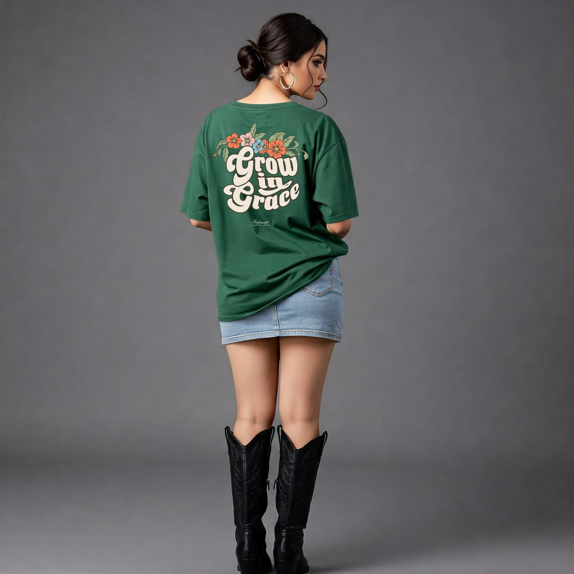 Woman wearing a green t-shirt with 'Grow in Grace' text and floral designs on the back, standing against a gray background.