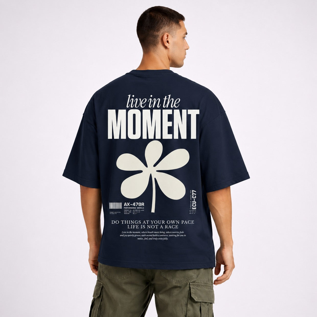 Man wearing a navy blue t-shirt with 'live in the moment' text and flower design on the back.