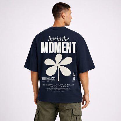 Man wearing a navy blue t-shirt with 'live in the moment' text and flower design on the back.