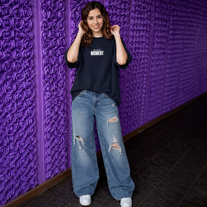 Woman wearing a black t-shirt and blue jeans standing against a textured purple wall.