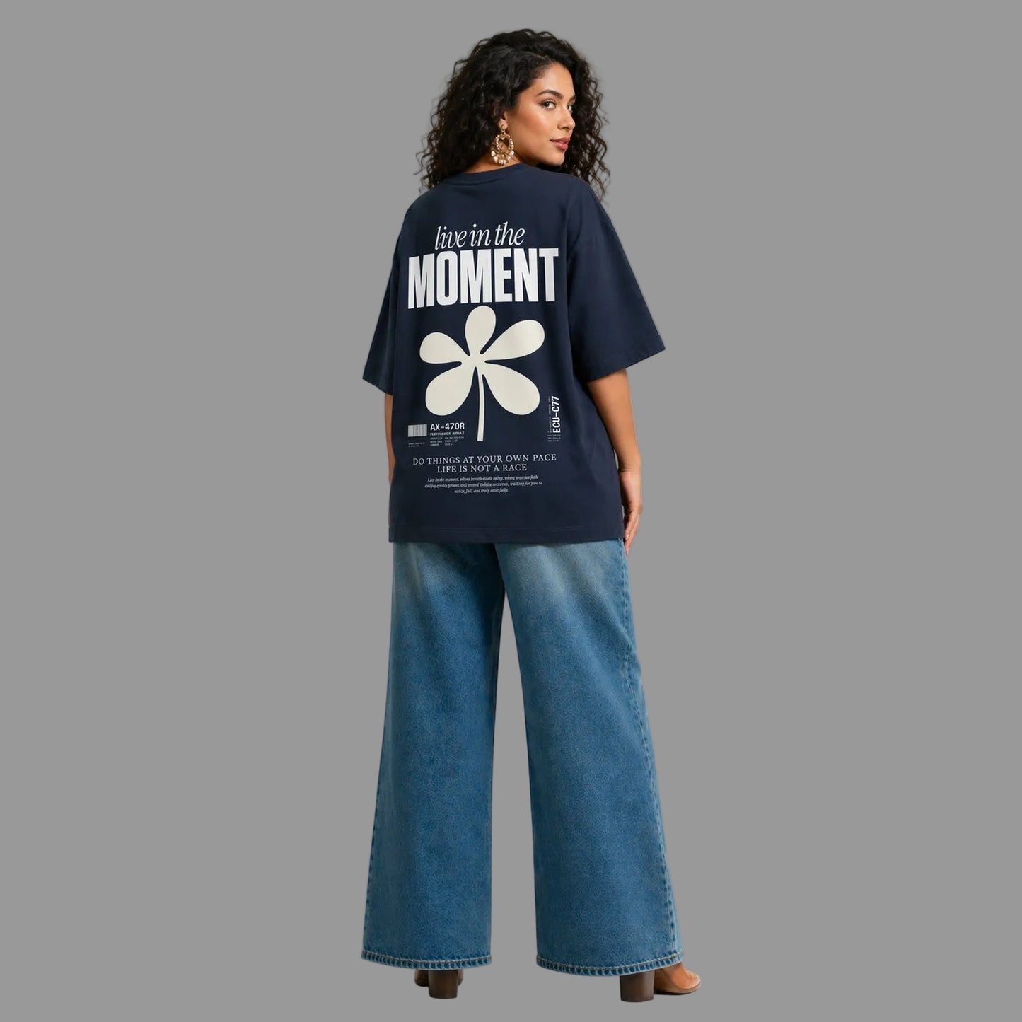 Woman wearing a navy blue t-shirt with a white flower design and text on the back, standing against a gray background.