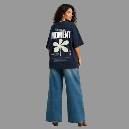 Woman wearing a navy blue t-shirt with a white flower design and text on the back, standing against a gray background.