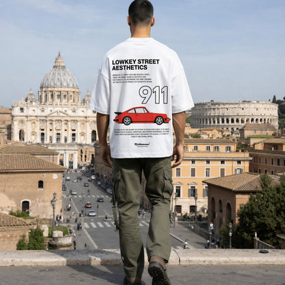 Person wearing a white t-shirt with text and graphics, standing in front of historical buildings in Rome.