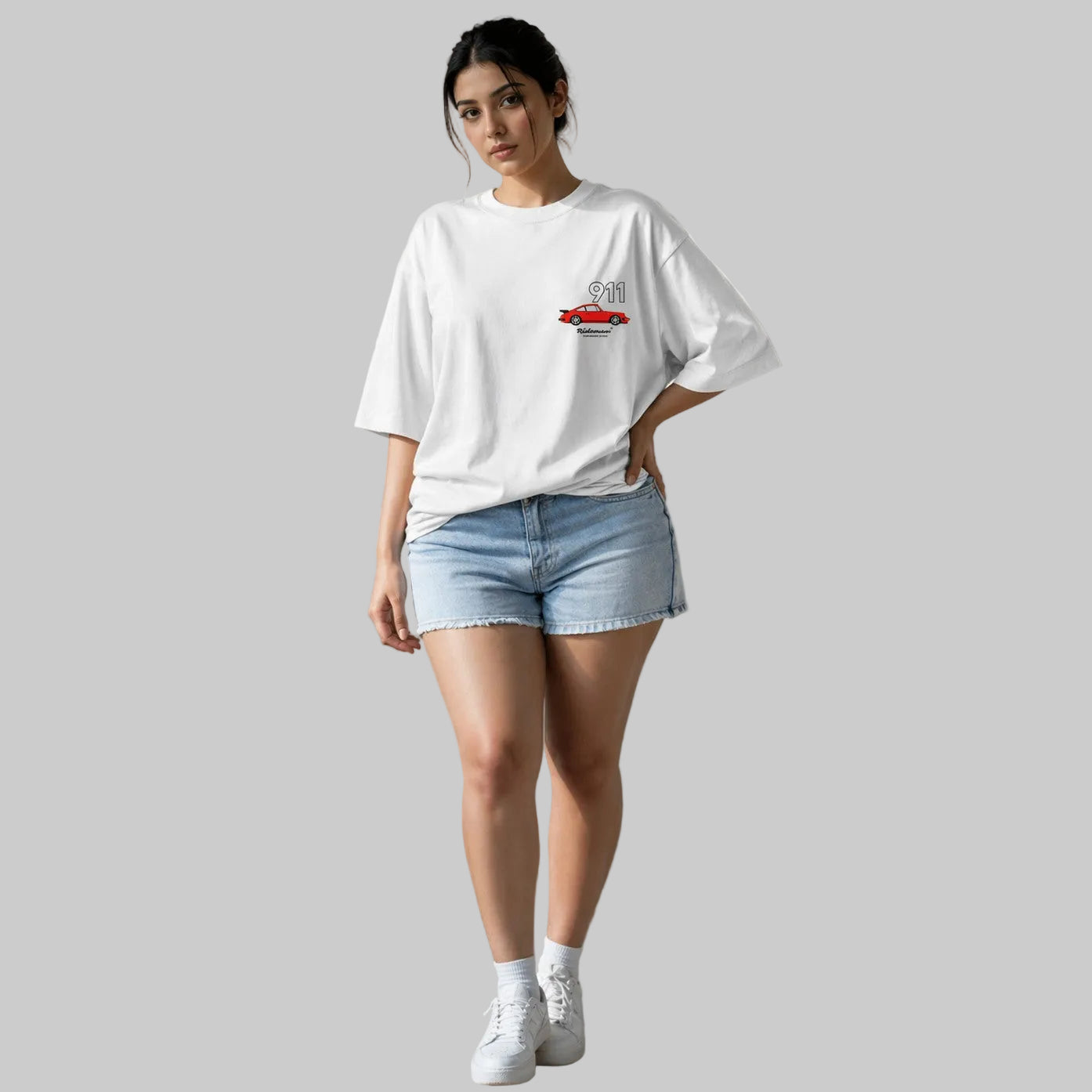 Woman wearing a white oversized t-shirt and denim shorts standing against a plain wall.