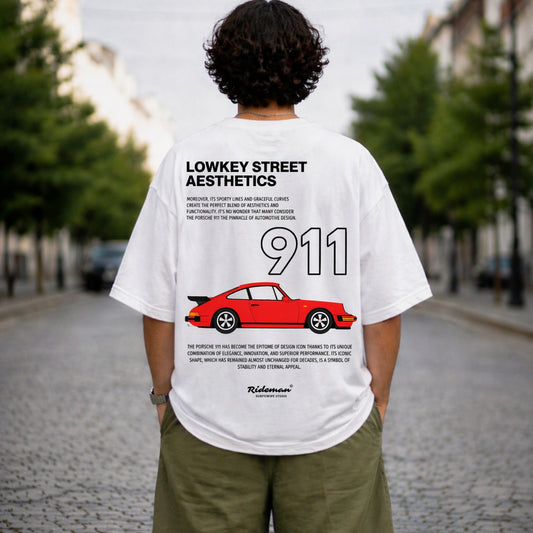 Person wearing a white t-shirt with 'LOWKEY STREET AESTHETICS' and a red Porsche 911 graphic on the back, standing on a street.