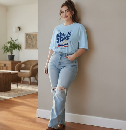 Woman wearing a light blue t-shirt and jeans standing indoors.