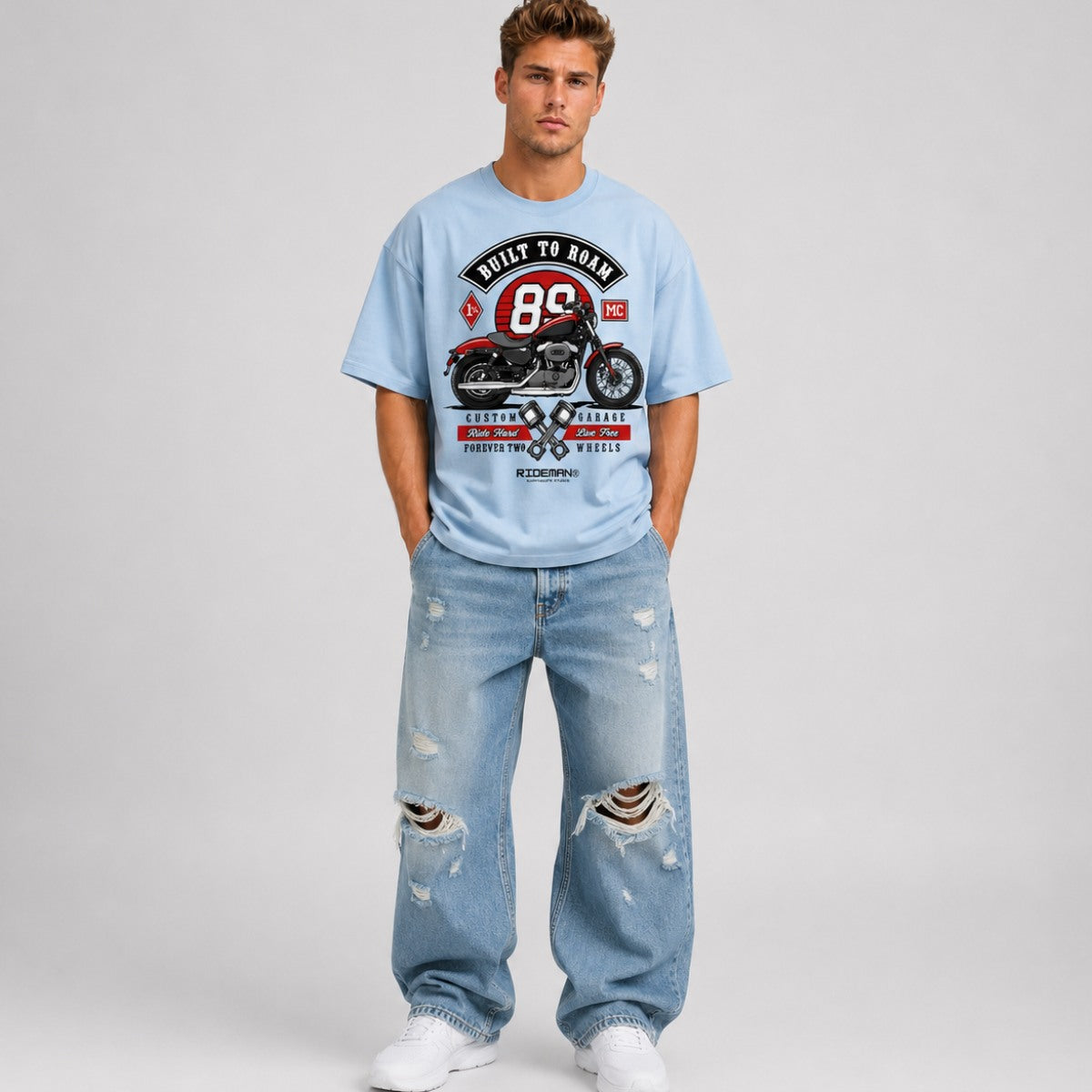 Man wearing a light blue t-shirt with a graphic design and distressed jeans on a plain background