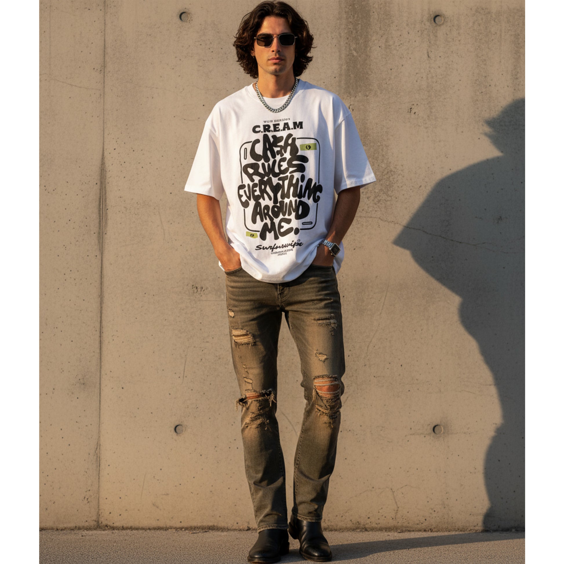 Man wearing a white graphic t-shirt and distressed jeans against a concrete wall.