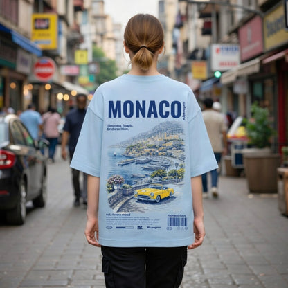 Person wearing a light blue t-shirt with 'MONACO' design on a city street.