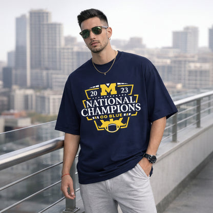Man wearing a navy blue t-shirt with '2023 National Champions' text and graphics, standing on a rooftop with cityscape background.
