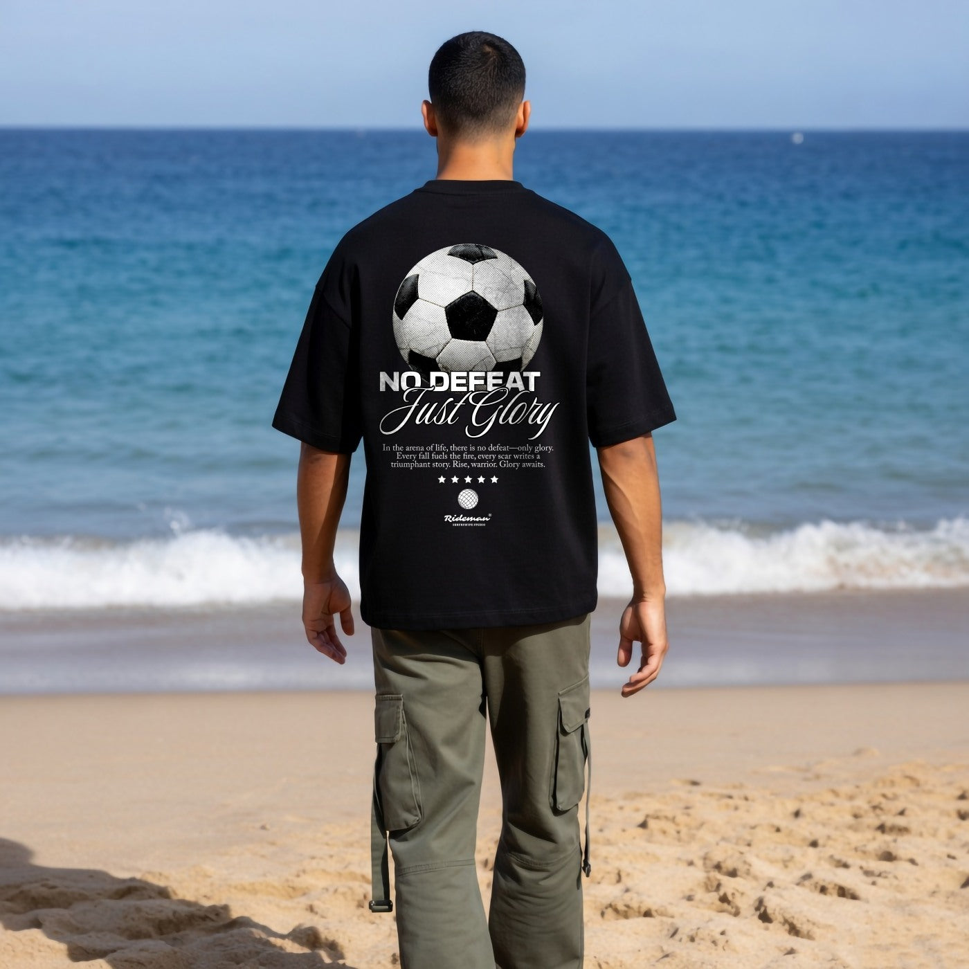 Person wearing a black t-shirt with a soccer ball design and text on a beach.
