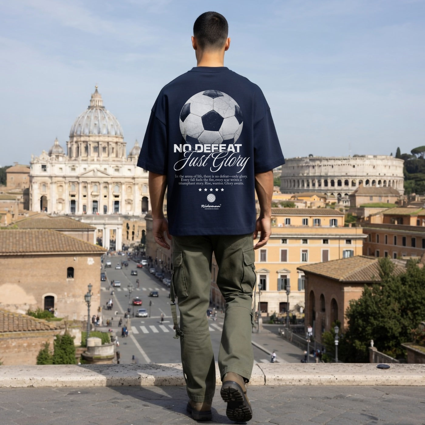Man wearing navy oversized football graphic t-shirt with No Defeat Just Glory print, standing near the Colosseum in Rome"