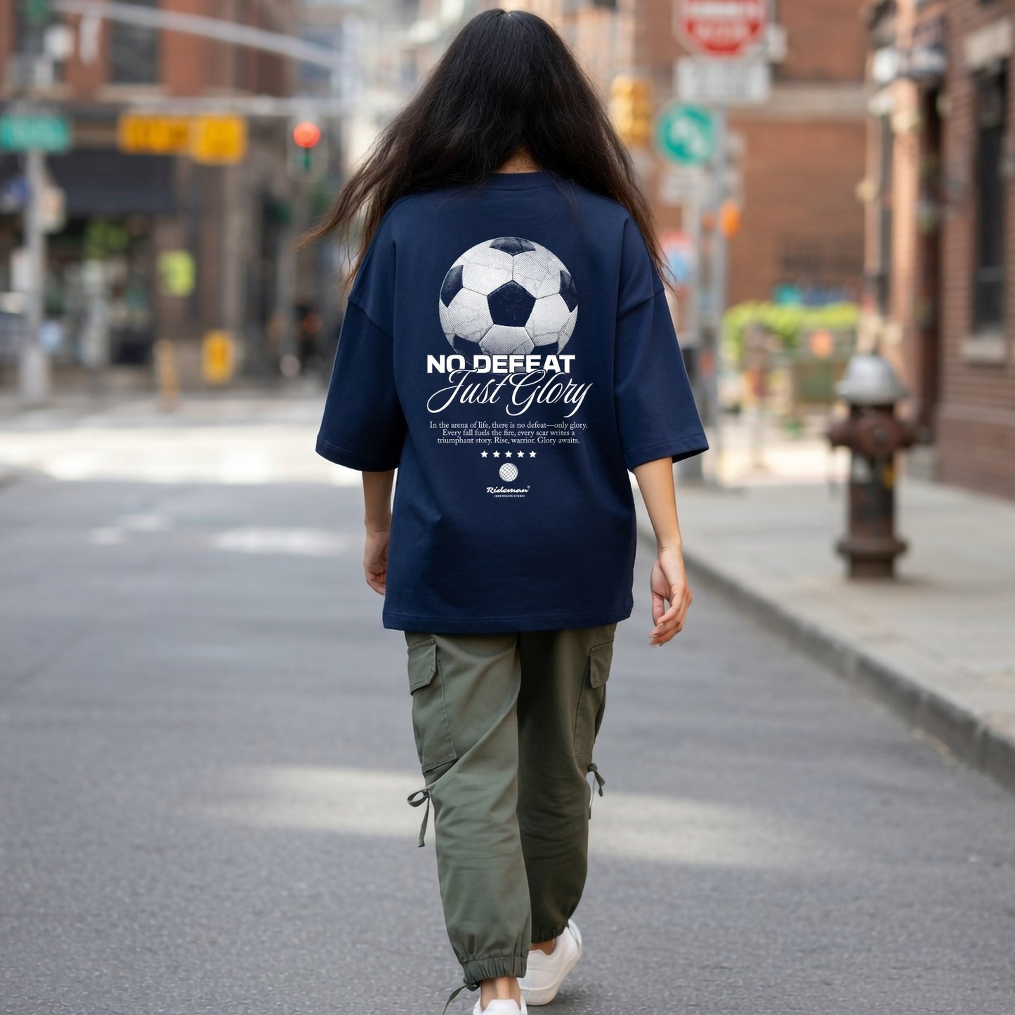 Person wearing a navy blue t-shirt with a soccer ball design and text on a city street.