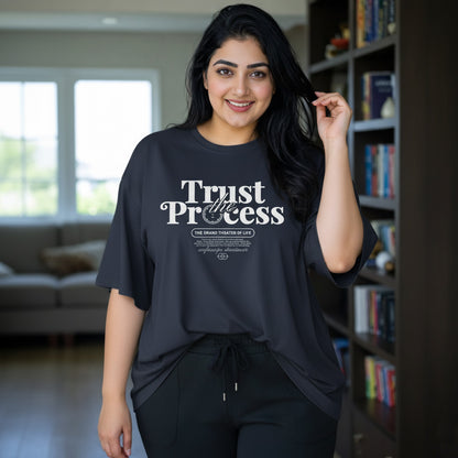 Woman wearing a black t-shirt with 'Trust the Process' text in a living room.