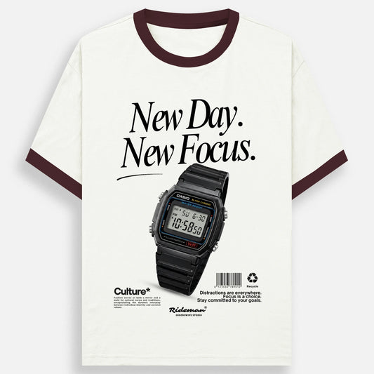 An off-white ringer t-shirt with dark brown trim on the collar and sleeve cuffs, featuring a graphic print of a black Casio watch and the text 'New Day. New Focus.