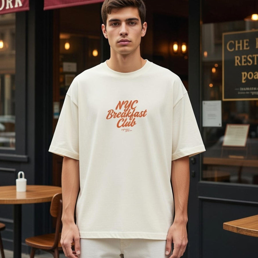 Man wearing a 'NYC Breakfast Club' t-shirt standing in front of a cafe.