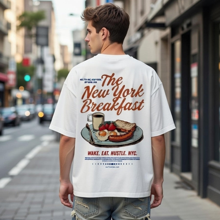 Person wearing a white t-shirt with 'The New York Breakfast' design on a city street.