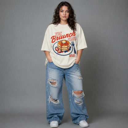Person wearing a 'The Brunch Club' t-shirt and ripped jeans on a gray background
