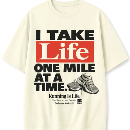 An off-white short-sleeve t-shirt with a bold graphic print on the front. The design features the text 'I TAKE Life ONE MILE AT A TIME.