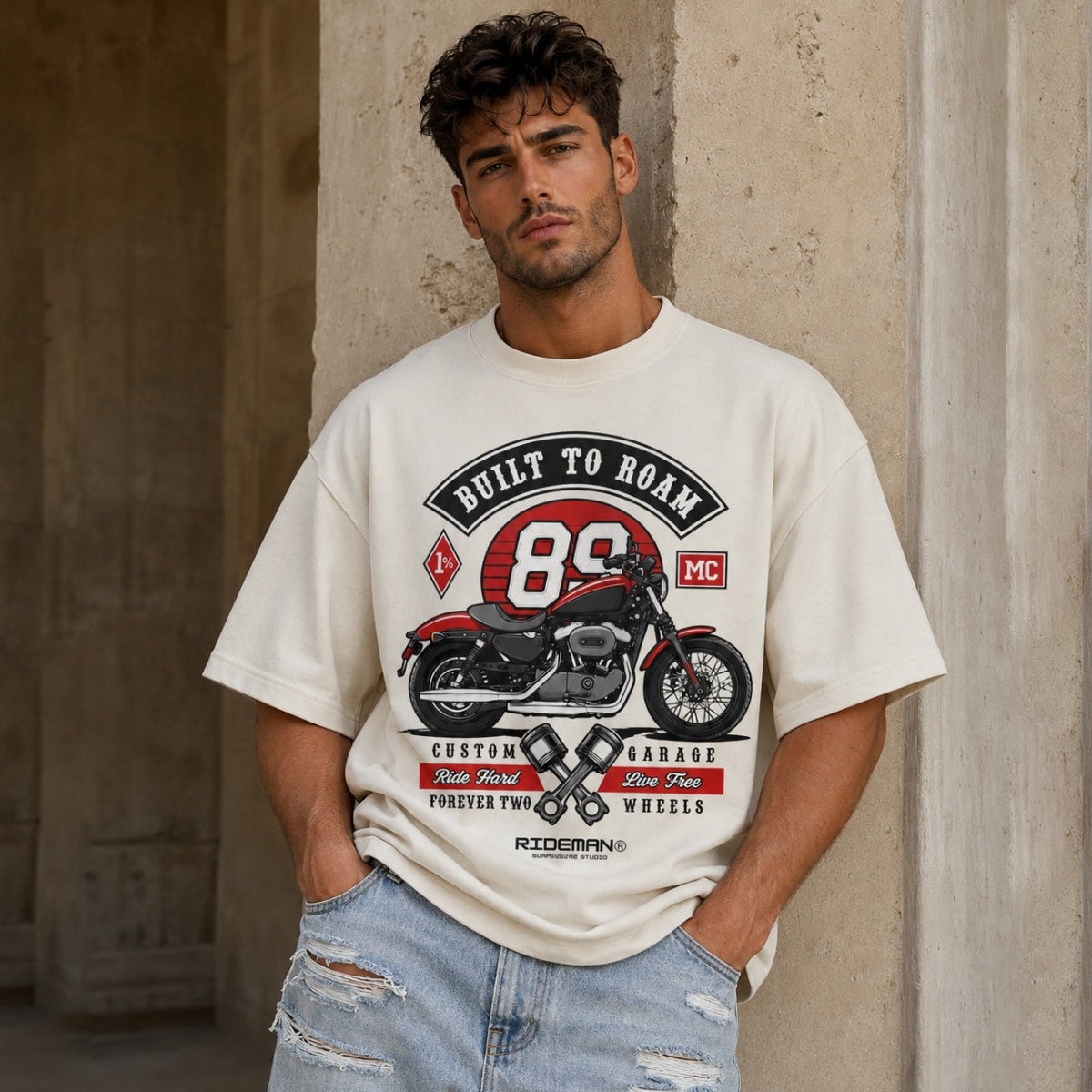 Man wearing a t-shirt with a motorcycle graphic and text against a textured wall.