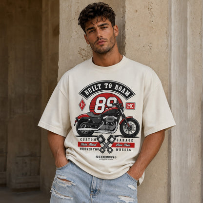 Man wearing a t-shirt with a motorcycle graphic and text against a textured wall.