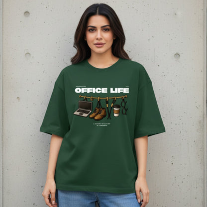 Woman wearing a green t-shirt with 'OFFICE LIFE' graphic design against a concrete wall.