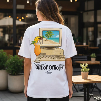 Person wearing a white t-shirt with a graphic design of a computer and beach scene, standing in an outdoor setting.