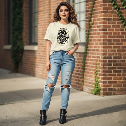 Woman wearing a beige t-shirt with text and ripped jeans standing in front of a brick wall.