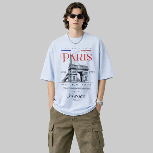 Man wearing a light blue t-shirt with Paris-themed design on a plain background